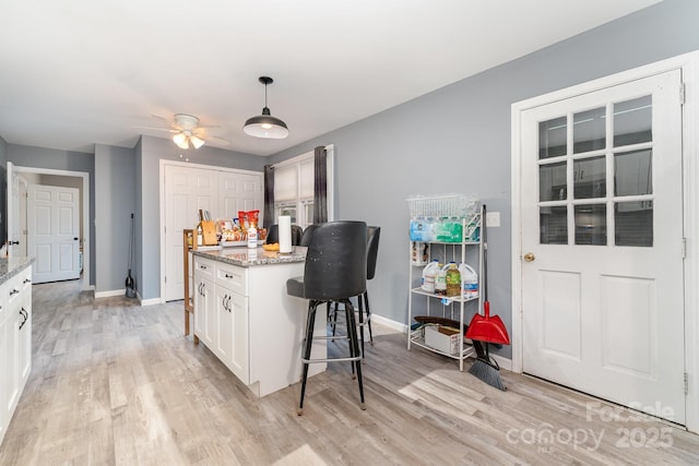 kitchen with a ceiling fan, white cabinetry, light stone counters, light wood finished floors, and baseboards