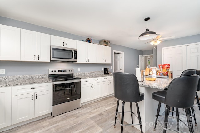 kitchen featuring light wood-style flooring, a ceiling fan, white cabinets, a breakfast bar, and appliances with stainless steel finishes