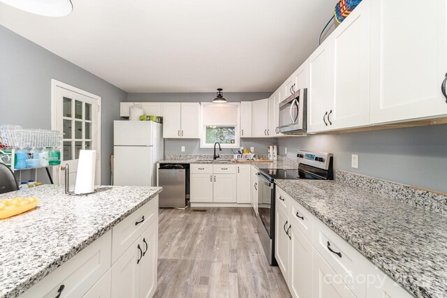 kitchen featuring white cabinets, a sink, light wood-type flooring, stainless steel appliances, and light stone counters