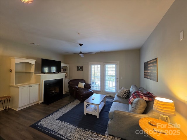 living area featuring a fireplace with flush hearth, dark wood-style flooring, and ceiling fan