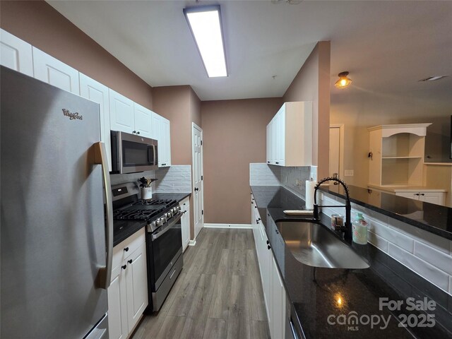 kitchen featuring a sink, decorative backsplash, light wood finished floors, white cabinets, and appliances with stainless steel finishes