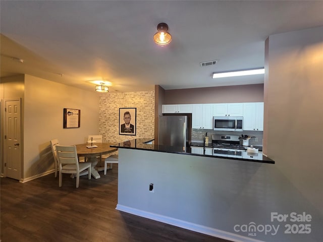 kitchen featuring dark wood-style floors, white cabinetry, dark countertops, visible vents, and stainless steel appliances