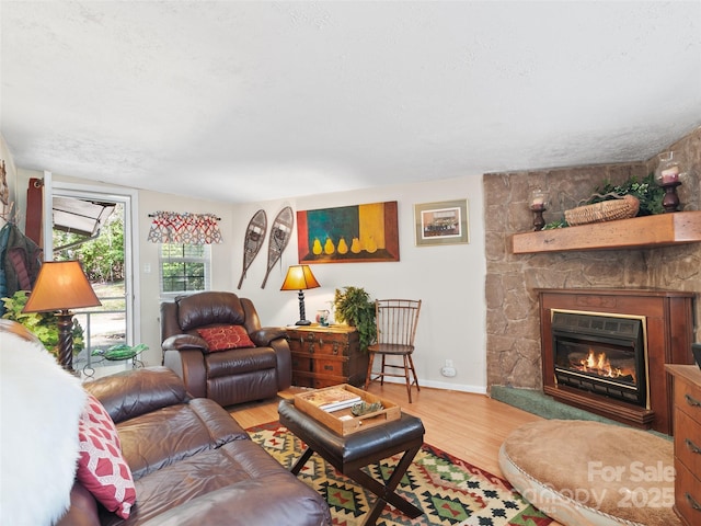 living room featuring a stone fireplace, wood finished floors, and baseboards