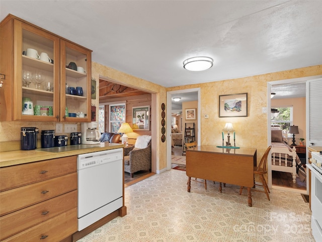 kitchen with glass insert cabinets, brown cabinetry, light countertops, white dishwasher, and light wood finished floors