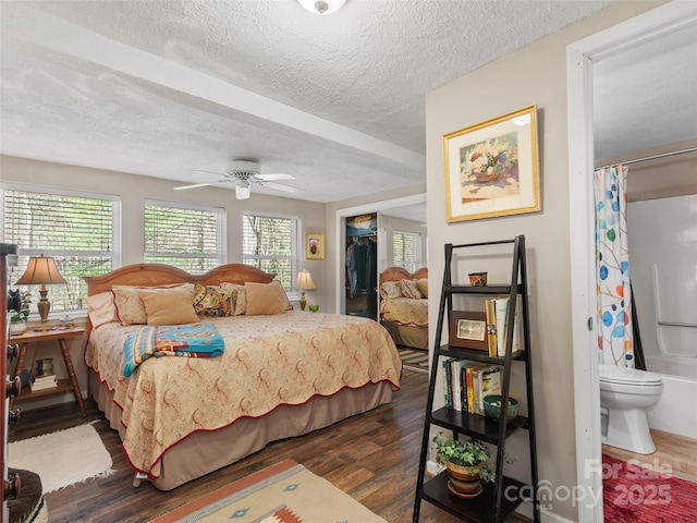 bedroom with a textured ceiling, a closet, connected bathroom, a walk in closet, and dark wood-style floors