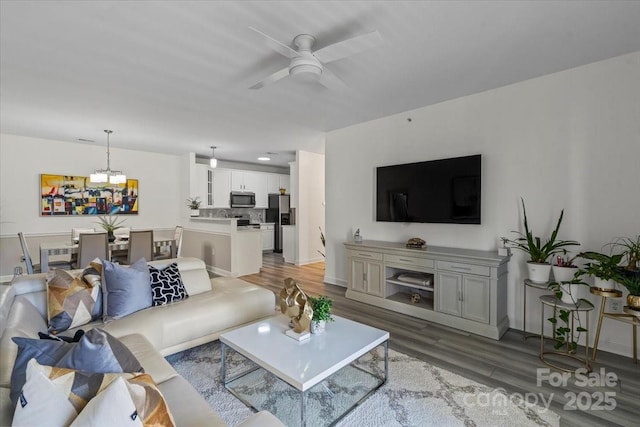 living room with baseboards, wood finished floors, and ceiling fan with notable chandelier