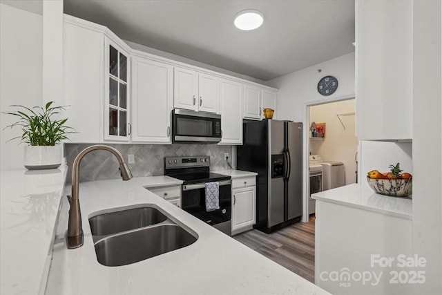 kitchen featuring stainless steel appliances, a sink, washing machine and clothes dryer, and white cabinetry