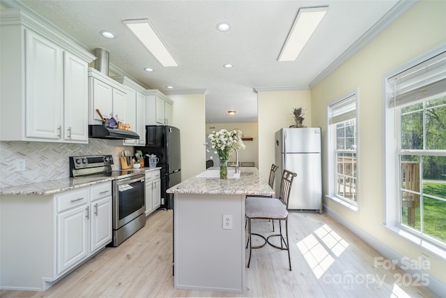 kitchen with a sink, under cabinet range hood, stainless steel appliances, and plenty of natural light