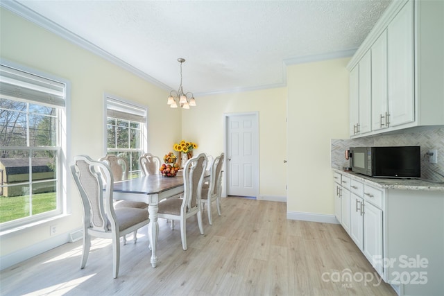 dining room featuring ornamental molding, light wood-style floors, baseboards, a textured ceiling, and a notable chandelier