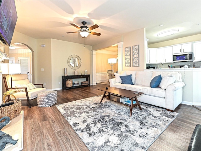 living room with ceiling fan, baseboards, dark wood finished floors, and arched walkways