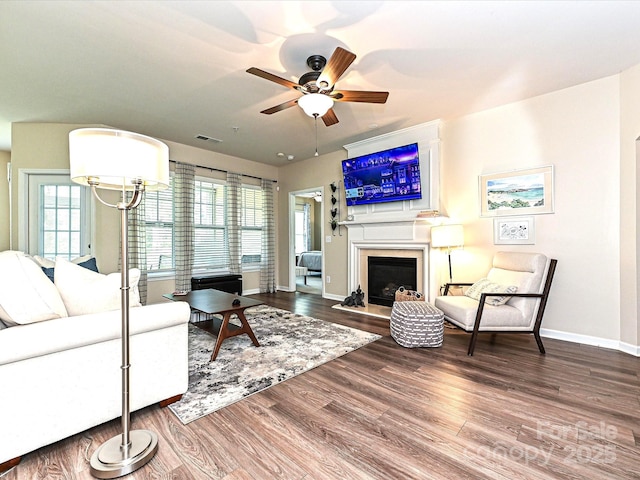 living area featuring wood finished floors, a large fireplace, ceiling fan, baseboards, and visible vents