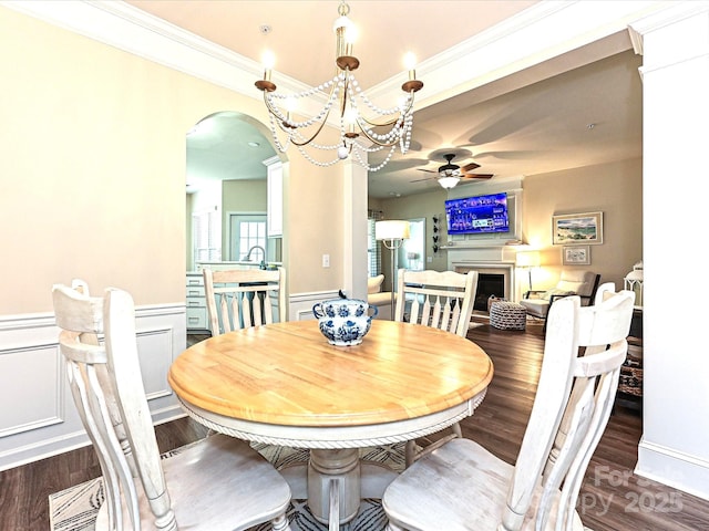 dining space featuring crown molding, a wainscoted wall, dark wood-style floors, arched walkways, and ceiling fan with notable chandelier