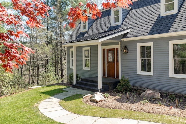 doorway to property featuring a porch, a shingled roof, and a lawn