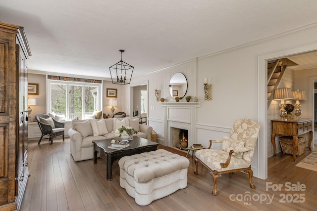 living area with ornamental molding, wood-type flooring, a chandelier, and a lit fireplace