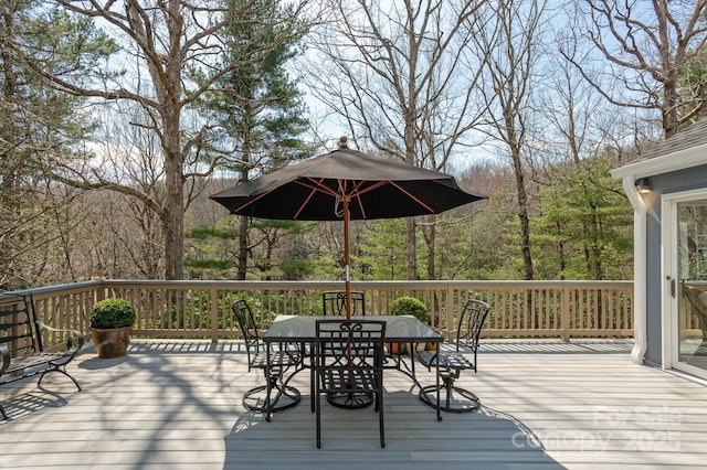 wooden terrace with outdoor dining space and a view of trees