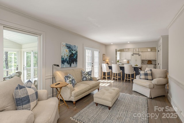 living area featuring crown molding, wood-type flooring, baseboards, and a healthy amount of sunlight