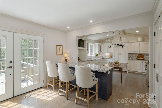 dining room featuring light wood-type flooring, ornamental molding, lofted ceiling, and visible vents