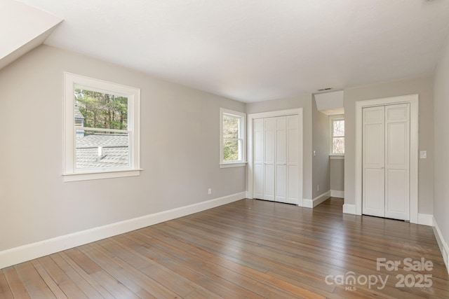 unfurnished bedroom with two closets, baseboards, visible vents, and hardwood / wood-style flooring