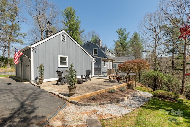 view of home's exterior with board and batten siding, a chimney, and a garage