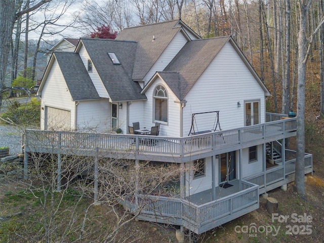 back of property with a shingled roof, a garage, a deck, and stairs