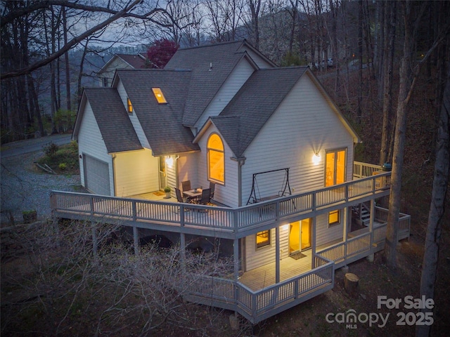 back of house featuring a shingled roof, a garage, and a wooden deck
