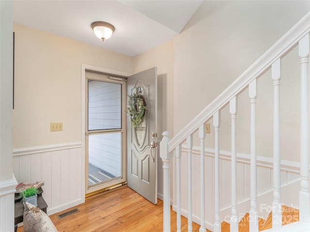 entrance foyer featuring stairs, light wood finished floors, visible vents, and a wainscoted wall