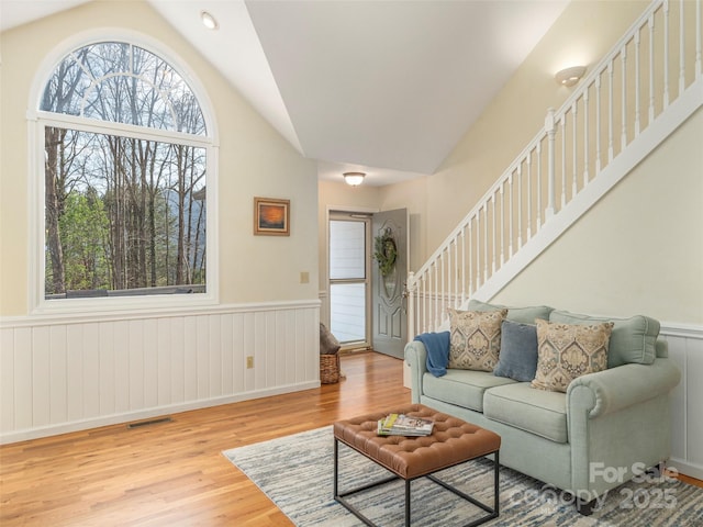 living area featuring visible vents, stairway, wainscoting, wood finished floors, and lofted ceiling