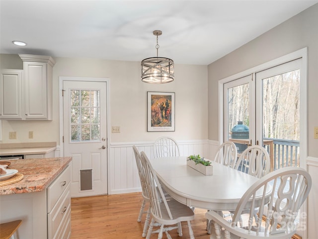 dining space with a wainscoted wall, light wood finished floors, and a chandelier