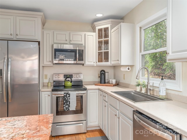 kitchen with light countertops, appliances with stainless steel finishes, a sink, and glass insert cabinets