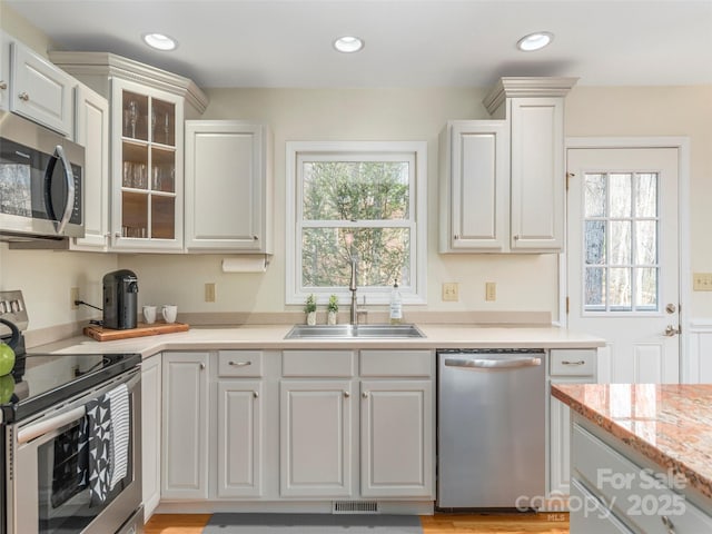 kitchen with recessed lighting, glass insert cabinets, a sink, and appliances with stainless steel finishes
