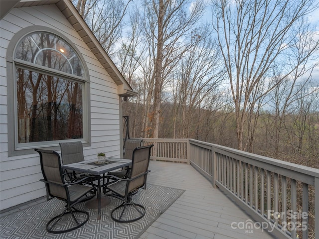 wooden deck with a forest view and outdoor dining area