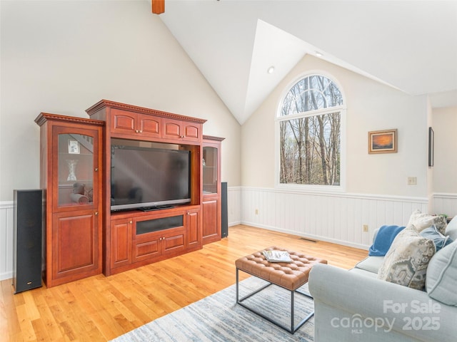 living area featuring visible vents, a wainscoted wall, light wood finished floors, and vaulted ceiling