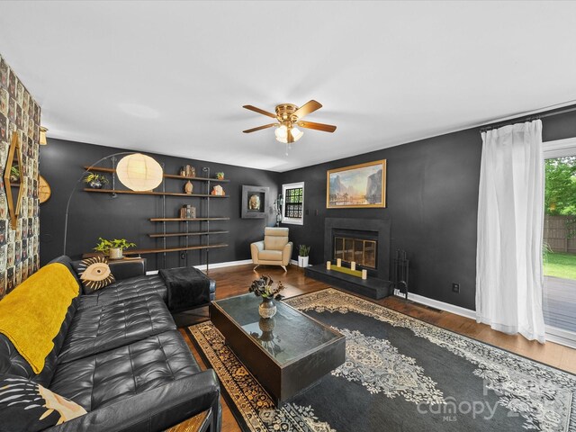 living area featuring a ceiling fan, a wealth of natural light, wood finished floors, and a glass covered fireplace