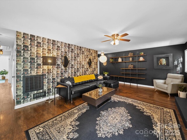 living area featuring ceiling fan, visible vents, baseboards, an accent wall, and wood finished floors