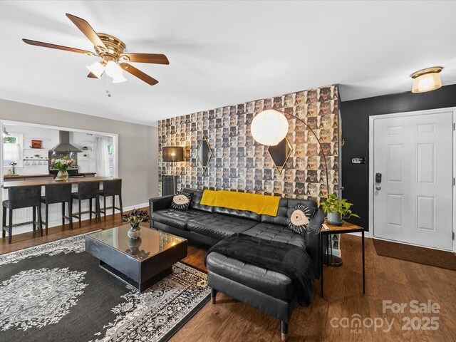 living room with an accent wall, ceiling fan, wood finished floors, and baseboards