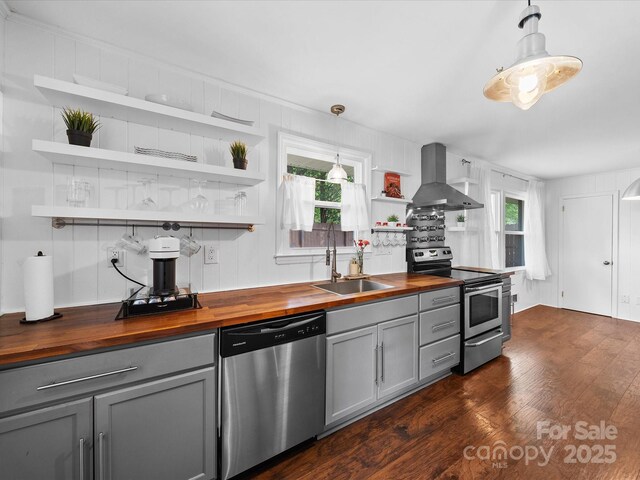 kitchen featuring gray cabinets, stainless steel appliances, wall chimney exhaust hood, and butcher block counters