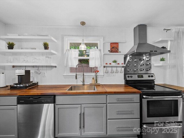 kitchen featuring wood counters, wall chimney range hood, open shelves, and appliances with stainless steel finishes