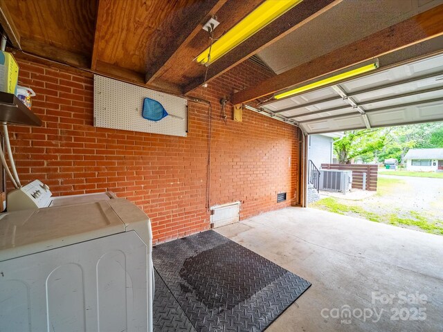 washroom with a garage, washing machine and clothes dryer, and brick wall