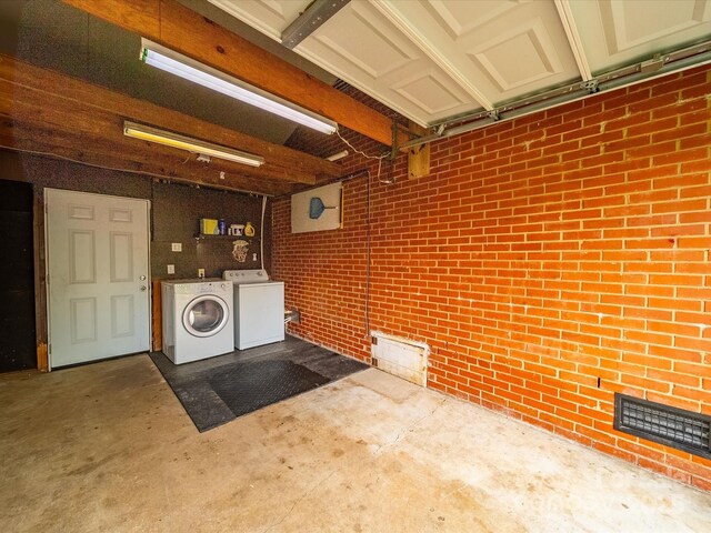 laundry area featuring a garage, brick wall, separate washer and dryer, laundry area, and visible vents