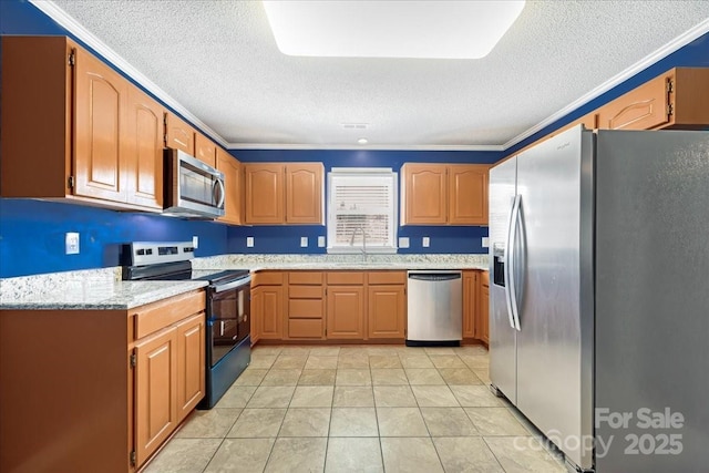 kitchen featuring light stone counters, light tile patterned floors, crown molding, appliances with stainless steel finishes, and a sink