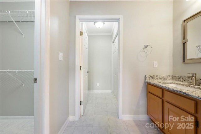 bathroom with a walk in closet, vanity, marble finish floor, and baseboards