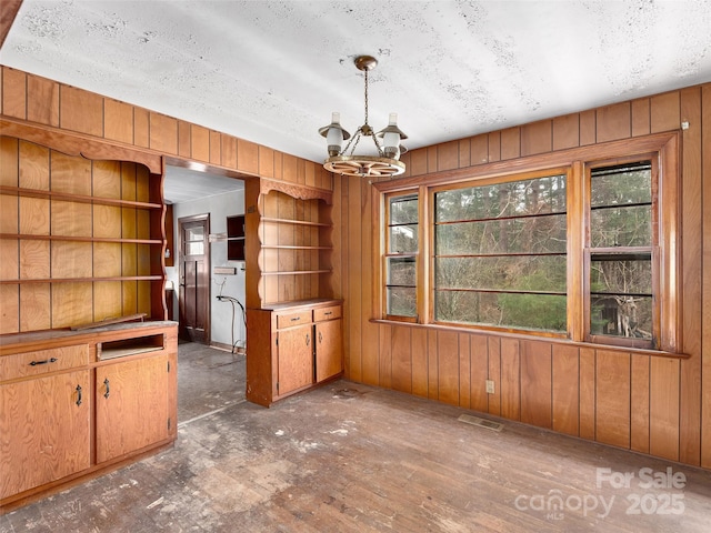 unfurnished dining area with wooden walls, visible vents, a textured ceiling, and an inviting chandelier