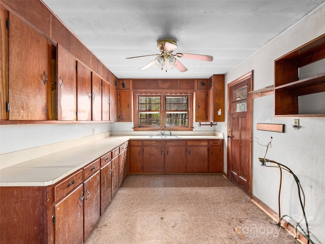 kitchen with a sink, light countertops, a ceiling fan, brown cabinetry, and light floors
