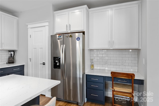 kitchen with white cabinets, backsplash, wood finished floors, light stone countertops, and stainless steel fridge