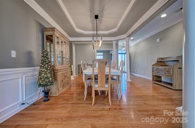 dining room featuring decorative columns, light wood-type flooring, a tray ceiling, and ornamental molding