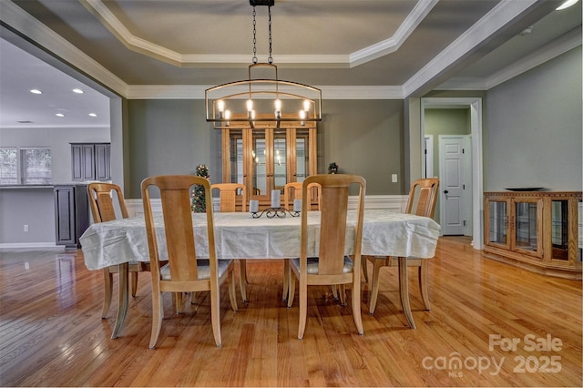dining room featuring light wood-style flooring, an inviting chandelier, crown molding, and a raised ceiling