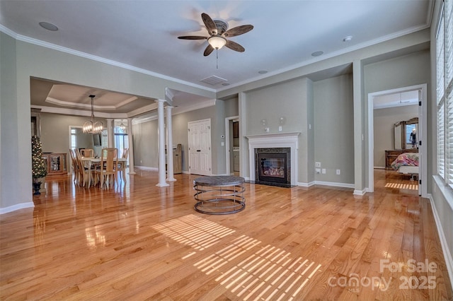 unfurnished living room featuring crown molding, ornate columns, a raised ceiling, a high end fireplace, and light wood finished floors