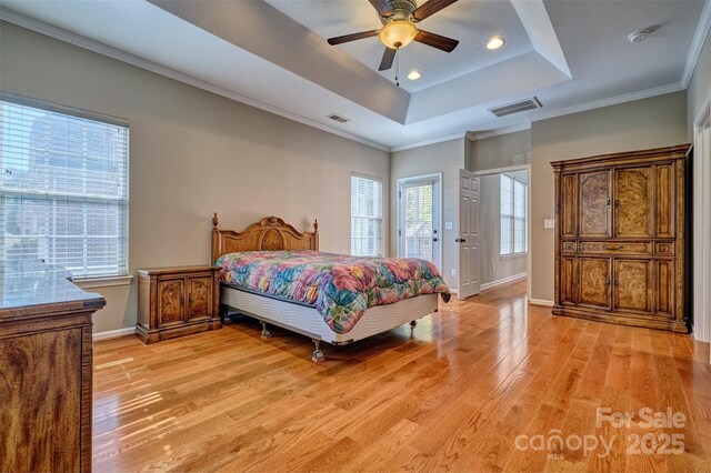 bedroom with light wood-type flooring, visible vents, a tray ceiling, and ornamental molding