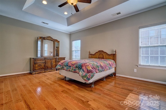 bedroom featuring visible vents, light wood-style flooring, a raised ceiling, and baseboards