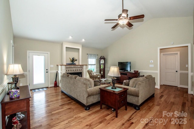 living area featuring a ceiling fan, light wood-style floors, a fireplace, and vaulted ceiling